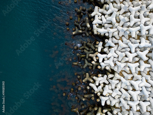 Heavy concrete tetrapods lined along the shoreline at a coastal area during daylight hours