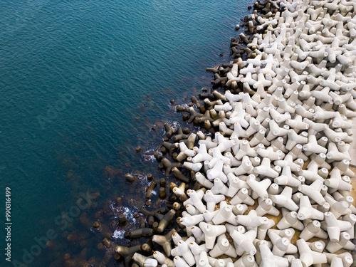 Heavy concrete tetrapods lined along the shoreline at a coastal area during daylight hours