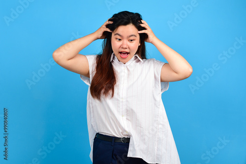 Portrait of a beautiful Asian businesswoman holding her head and screaming isolated on blue bakcround. Depressed woman shouting on blue bright background