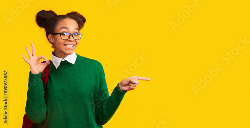 Great Choice. Excited afro teenage girl pointing at copyspace, showing ok sign, panorama, yellow wall