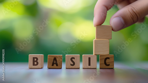 Hand stacking wooden blocks spelling "BASIC" with a green blurred background, symbolizing simplicity and fundamentals.