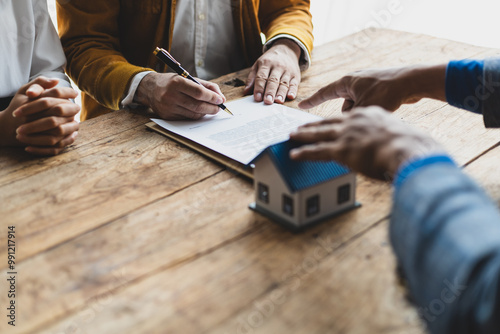 The real estate agent is explaining the terms of the home purchase agreement contract and the client legally signs the contract. Couple is signing a home sales contract with the salesman.