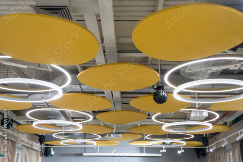 This contemporary ceiling design features elegant circular lights complemented by acoustic panels, all adorned in a vibrant shade of yellow