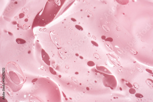 Close-up shot of pink liquid cosmetic gel or serum makeup swatches with a glossy, shiny texture on a smooth pink background