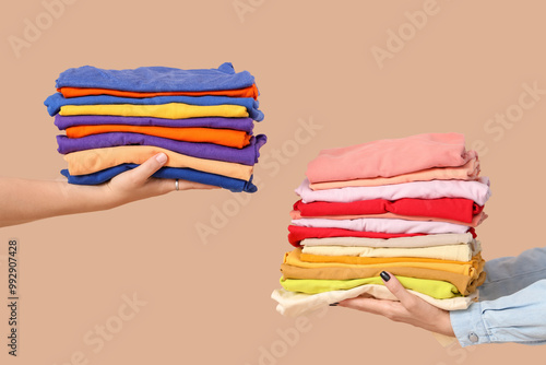 Young women with stacks of colorful clothes on beige background