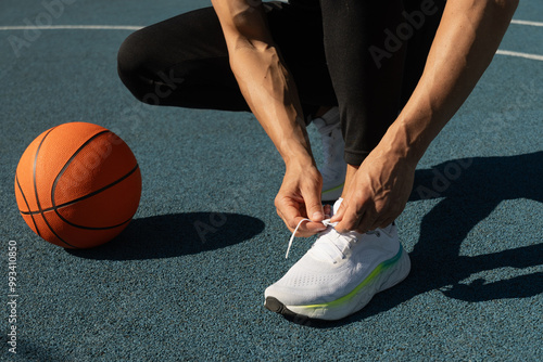 Close up basketball player tying sports shoes in basketball court outdoors. Last preparation. Summer team game.