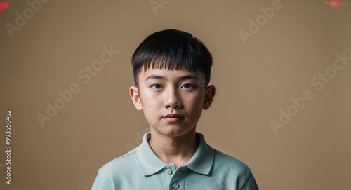 Focused Asian teenage boy with buzz cut wearing polo shirt on plain beige background