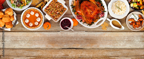 Thanksgiving turkey dinner. Overhead view top border on a rustic wood table banner background. Turkey, mashed potatoes, stuffing, pumpkin pie and sides.