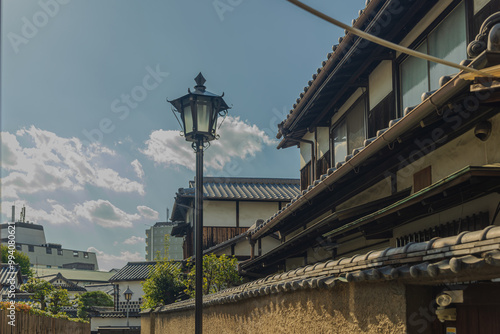  A street lamp is situated in front of traditional Japanese buildings under a clear sky with clouds.