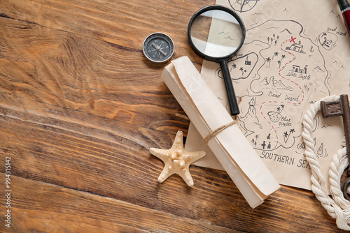 Treasure map with magnifier, scroll and compass on brown wooden background