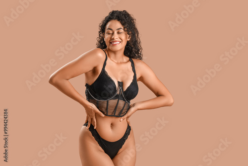 Beautiful young happy African-American woman in stylish lace lingerie on beige background