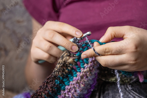 Young womans hands crochet colorful yarn with crocheting hook. Closeup details of handmade needlework art project and creative crafting techniques. Handmade textile artist nitting with yarn.