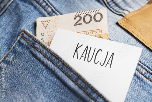 White card with a handwritten inscription "Kaucja", put into the pocket of blue pants jeasnow, next to Polish banknotes PLN (selective focus), translation: Bail