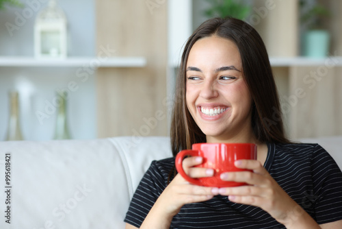 Happy woman smiling drinking coffee at home looking at side