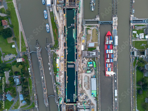 Topdown Aerial drone image of large cargo container ship carrier in lock sluice complex under construction in Brunsbüttel Germany at entrance of nord ostsee kanal or Kiel canal with small sailboat