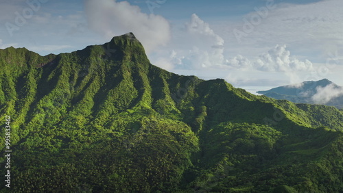 Sunny tropical island green rainforest mountain peaks. Showcasing vibrant colors and fluffy clouds. Exotic and unspoiled travel destination. Remote exotic wild nature. Drone shot natural background