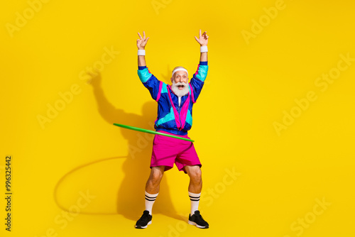 Full body portrait of eccentric aged man spinning hula hoop empty space workout retro sportswear isolated on yellow color background