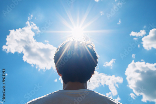 Back view of man looking into sun in blue sky