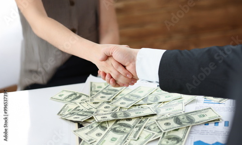 Close-up of man and woman shake hands over stack of dollars currency transaction of powers. People agreed on price. Business, big money, investment concept