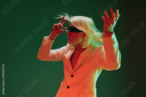 Stylish performer with long white hair, wearing a blindfold, posing dramatically in an artistic green and red background, showcasing creativity and expression through fashion and movement