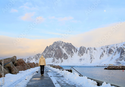 Giovane donna con vestiti invernali cammina sul molo di Bleik, Andoya. Isole Vesteralen, Norvegia