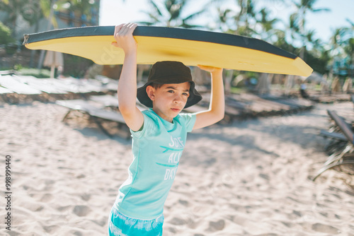 A little boy carrying a boogie board over his head at the beach on summer vacation. 