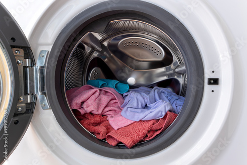 Colourful load of clothes and towels in a washing machine drum with open door