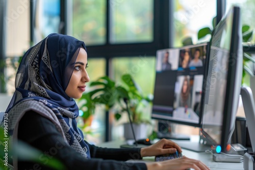 A woman wears a headscarf and works on her computer, possibly at home or in an office