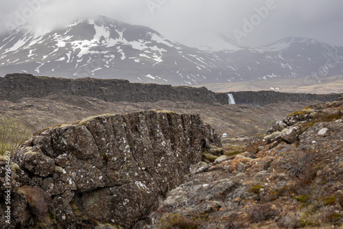 landscape of Þingvellir (Thingvellir) National Park, with Öxarárfoss and snow covered mountains on a cloudy, rainy day, Iceland