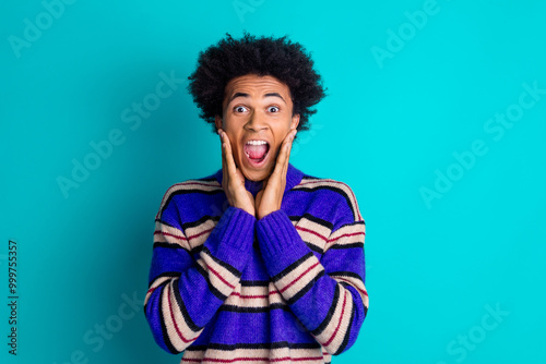 Photo of horified frightened man guy with wavy hairstyle dressed knitwear sweater scream hands on cheeks isolated on blue color background