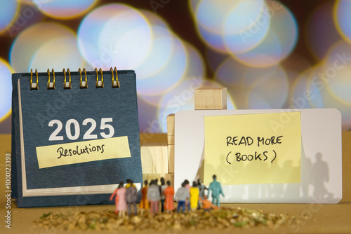 2025 calendar with a sticky note labeled "Resolutions" and another note with the message "read mores books" on a card. Small figurines of people stand in front of the display