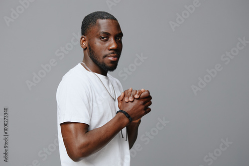 Stylish young man in casual white shirt with hands clasped, looking confidently at the camera against a neutral gray background Modern fashion portrait capturing a relaxed vibe