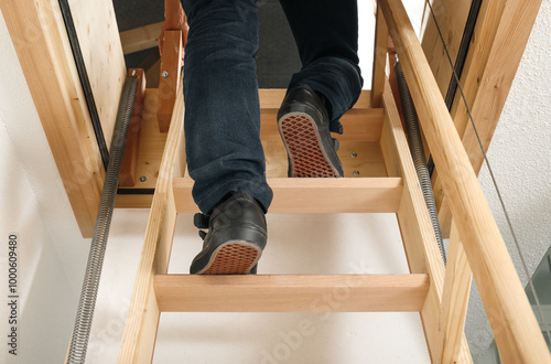 Back view of person using loft ladder or attic ladder. Woman climbing or going up loft sliding ladder to access attic space or loft. Space saving storage space. Selective focus. Lucerne, Switzerland.