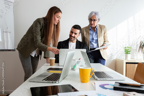 Group of coworkers working together solving problem looking at laptop and paper documents in the office.