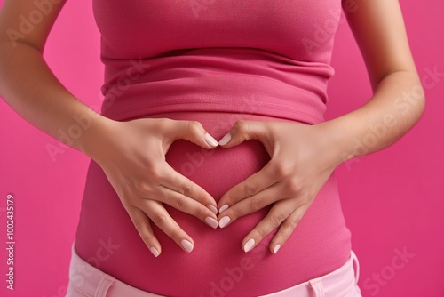 Female hand forming heart shape near woman belly on pink background. Close-up of healthy digestion concept. Woman abdominal area highlighted in pink, symbolizing balance and care for internal organs.