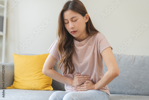 Flatulence asian young woman intolerance hand in stomach ache, suffer from food poisoning, abdominal pain and colon problem, gastritis or diarrhoea when at home. Patient belly, abdomen or inflammation