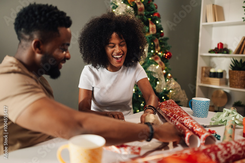 Smiling african american couple wrapping gifts together near Christmas tree.