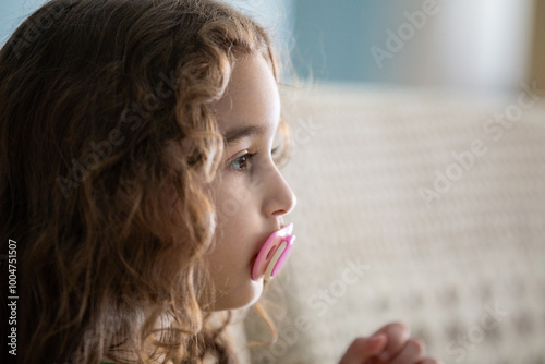 Close up no rosto de uma criança, menina, de perfil, com chupeta na boca, no ambiente doméstico.