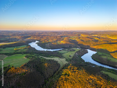 An aerial view of the Vltava River winding through the rolling hills of Czechia, bathed in the golden light of sunset.