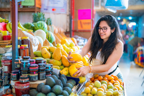 Young Latina woman happily picking mangoes at a vibrant market in Mexico City, Mexico.