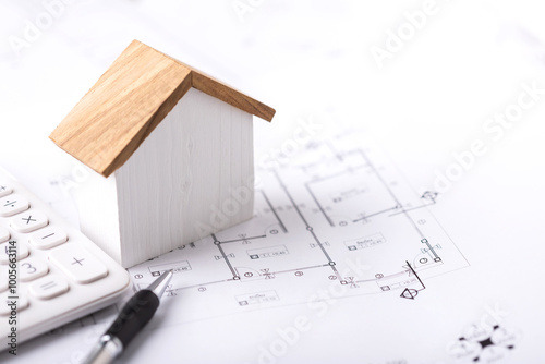 Concept of budgeting for home construction, with a house model, calculator, and construction plans placed on a table, symbolizing financial planning for building a home