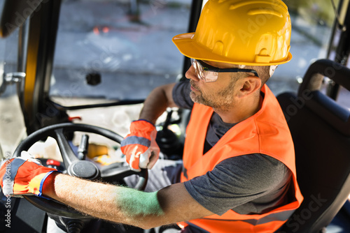 Construction worker operating heavy machinery at a job site during daytime wearing safety gear and focusing on the task