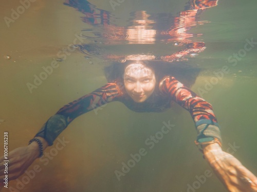 A young woman in wetsuit freediving, free diving, breath-hold swimming under water. Smiling swimmer who dives. Summer vacations, healthy lifestyle, amateur sport, leisure activity concepts