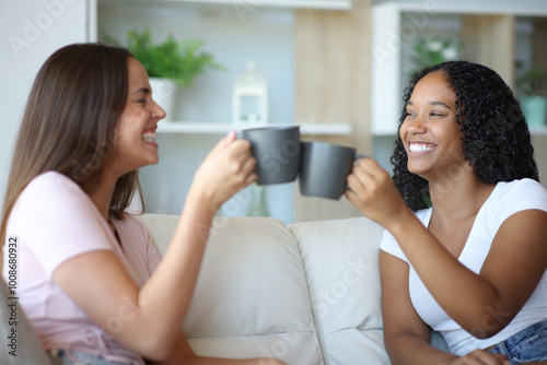 Happy interracial roommates toasting talking at home