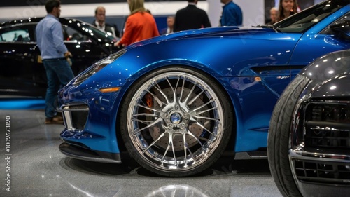 Blue sports car exhibiting chrome alloy wheels at a car show with people in the background