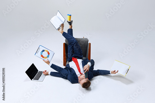 Businessman lying on ground, his lags in multiple directions, managing papers, laptop, and phone calls. Chaos meets productivity. Concept of business, work overload, multitasking, corporate stress