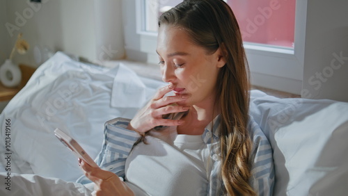 Dreamy lady reading sms on mobile phone comfortably resting at white bed closeup