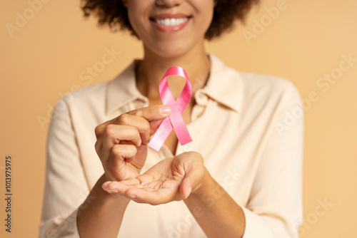 Smiling young woman holding pink ribbon for breast cancer awareness