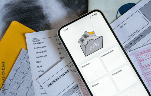 Ein Smartphone auf dem gerade eine elektronische Patientenakte angezeigt wird, liegt auf medizinischen Dokumenten, horizontal