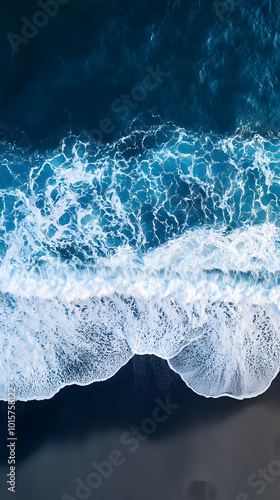 a teal and blue sapphire wave crashes onto a dark, black sandy beach, captured from a bird's eye view